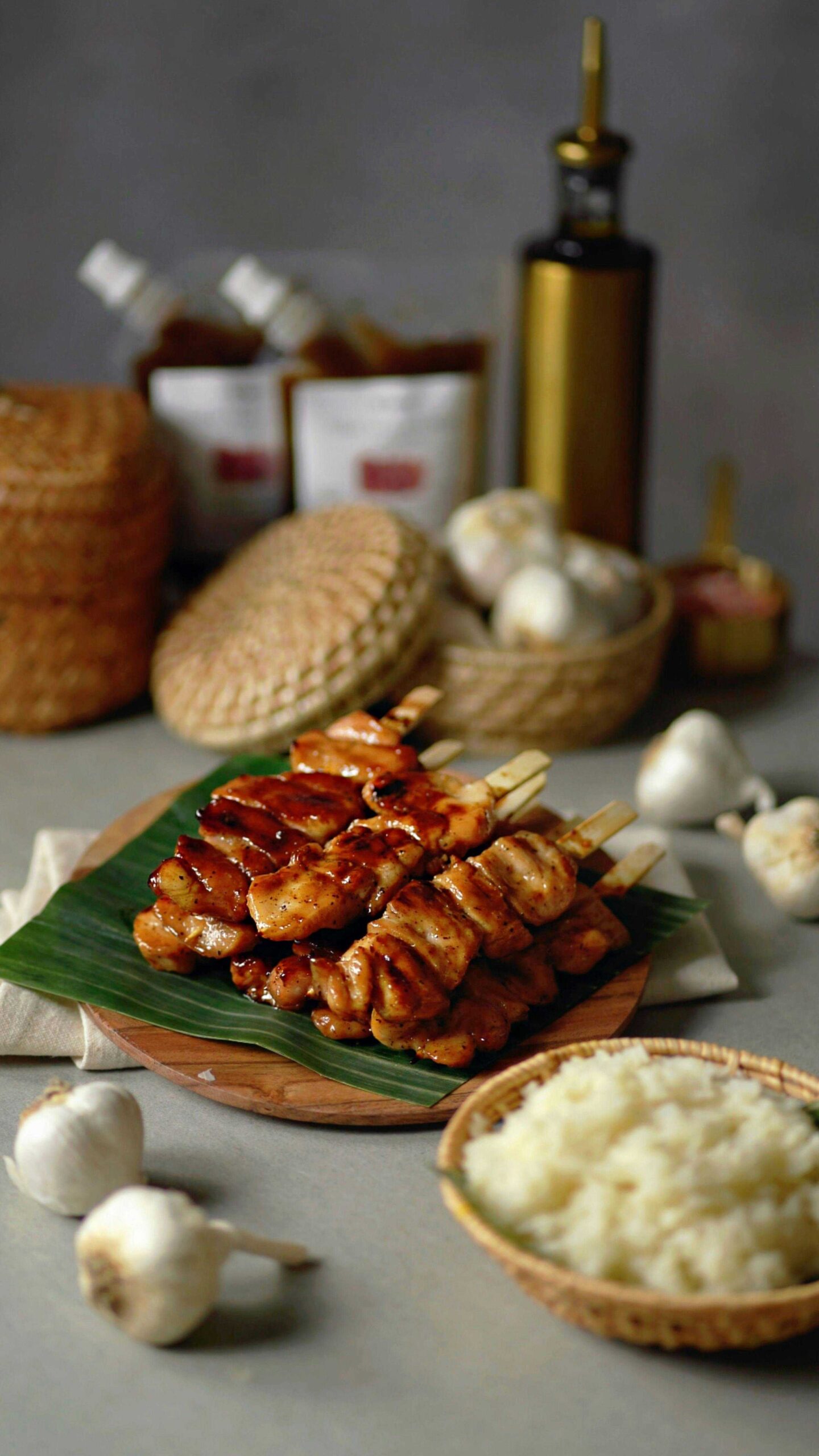 Juicy garlic Parmesan chicken skewers glazed with a rich sauce, served on a wooden plate with a banana leaf, fresh garlic, and a bowl of rice.