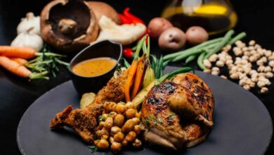 A beautifully plated garlic parmesan chicken dish served with crispy roasted chickpeas, breaded chicken, grilled vegetables, and a side of flavorful dipping sauce. Fresh ingredients like garlic, mushrooms, carrots, green beans, potatoes, and chickpeas are arranged in the background.