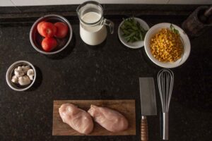 Raw-chicken-breast-orzo-tomatoes-garlic-onions-and-seasonings-on-a-wooden-board